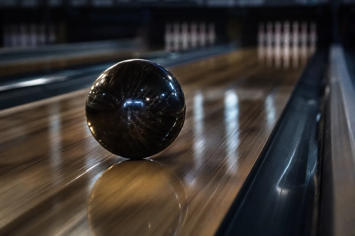 Boule de bowling sombre en pleine trajectoire sur une piste huilée, reflets lumineux sur le vernis