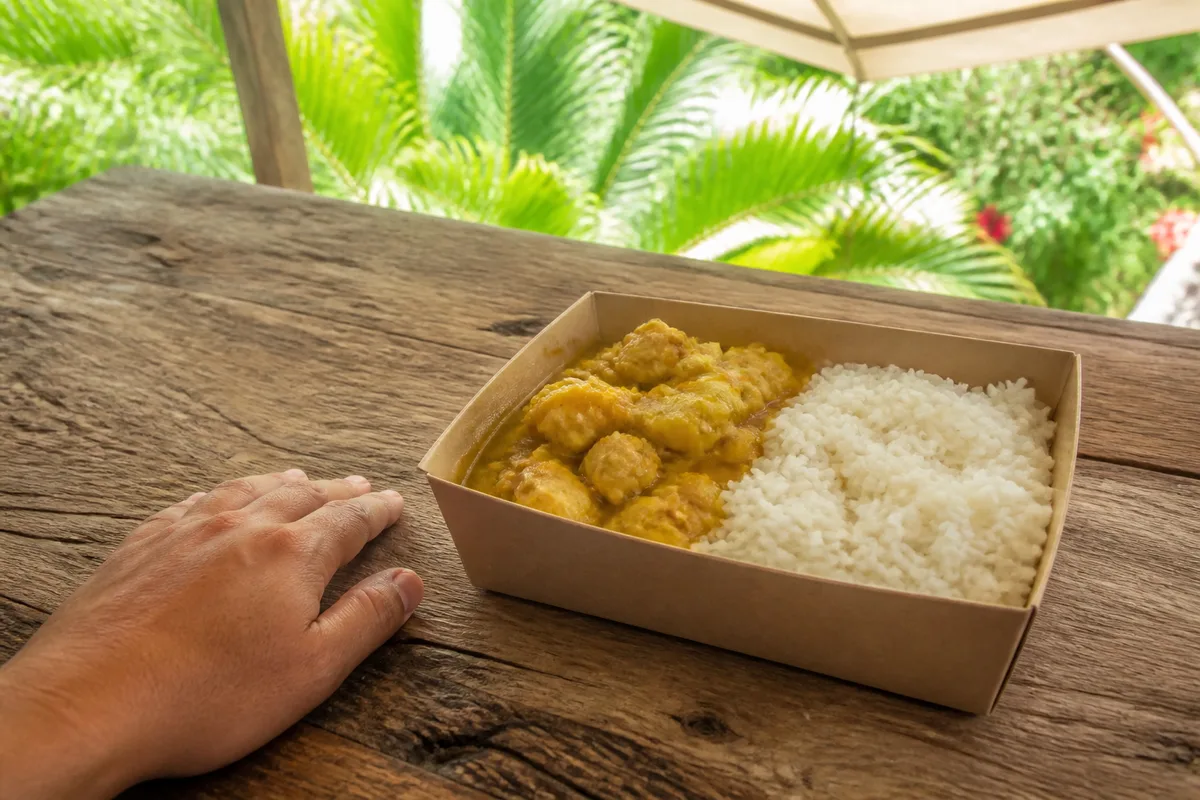 Barquette de colombo et riz posée sur une table en bois brut par une main